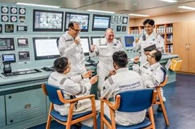 Six male MISC ship officers in a control room celebrating success.