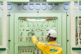 Engineer in yellow MISC uniform operating control panels in a ship's engine room.